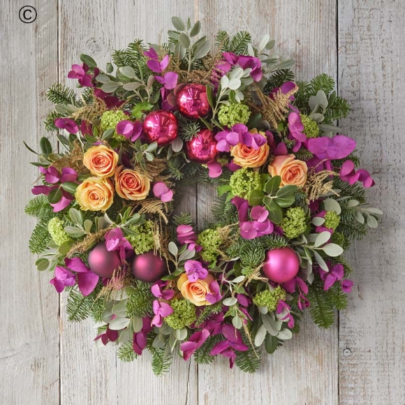 christmas wreath with purple and yellow blooms, pink christmas baubles, and fresh foliage