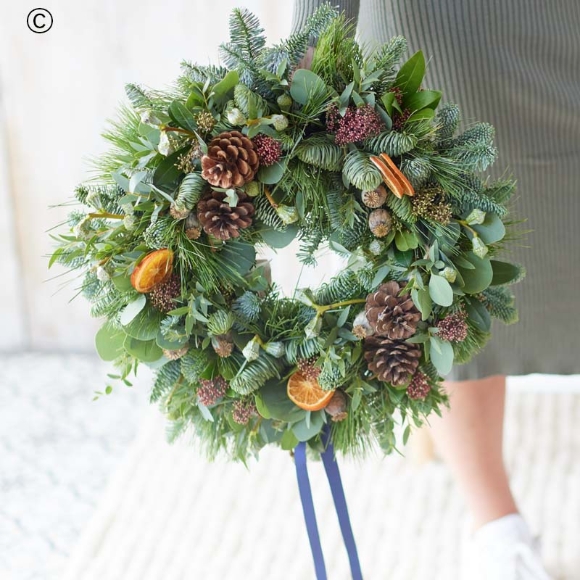 christmas wreath featuring fresh blooms and foliage with shades of red and green, and peach and cream highlights and pops of burgundy and cerise