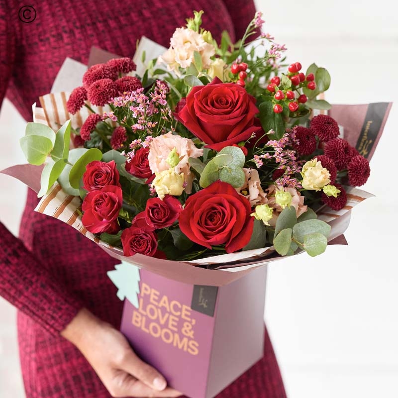 festive gift box with blooms in red and green, with peach and cream highlights and pops of burgundy and cerise