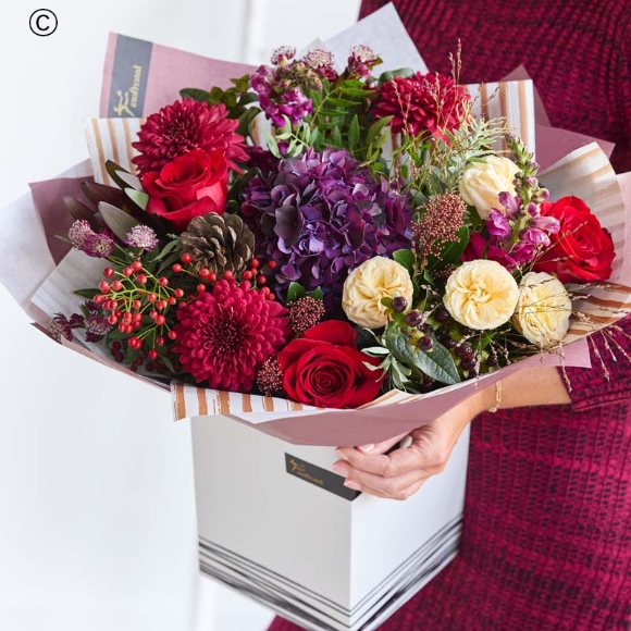 larger Christmas bouquet mix of luxurious flowers featuring blooms in shades of red and green, with peach and cream highlights and pops of burgundy and cerise