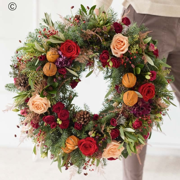 Christmas door wreath with fresh festive flowers in shades of red and green, with peach and cream highlights and pops of burgundy and cerise