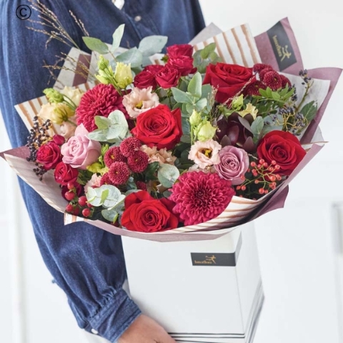 large festive bouquet of luxurious blooms in red and green, with peach and cream highlights and pops of burgundy and cerise