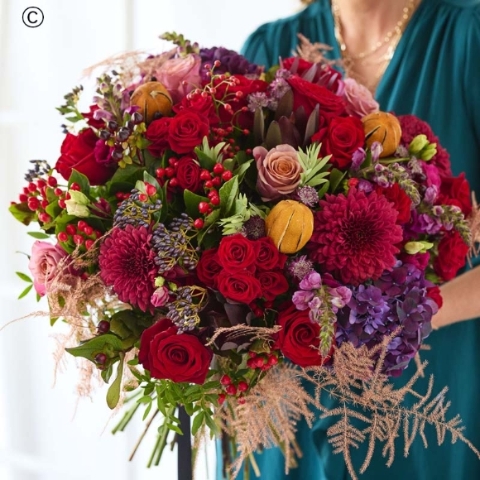  large Christmas bouquet featuring flowers in red and green, with peach and cream highlights and pops of burgundy and cerise