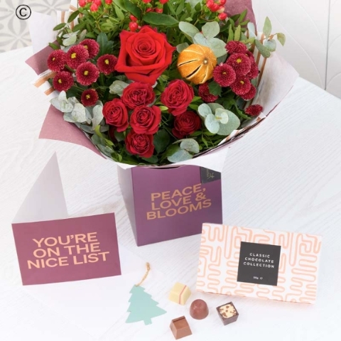 festive gift box featuring blooms in red and green, with peach and cream highlights and pops of burgundy and cerise, a festive card and chocolates