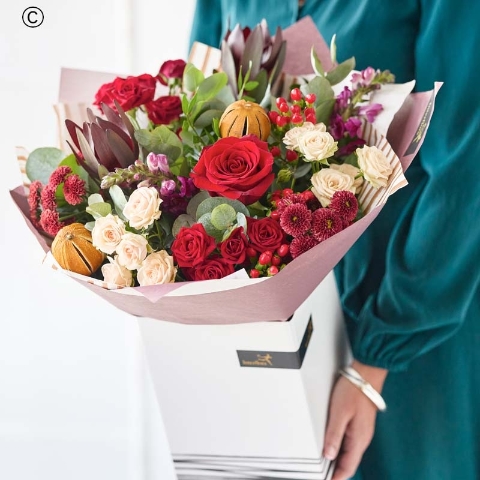 bouquet of blooms in red and green, with peach and cream highlights and pops of burgundy and cerise