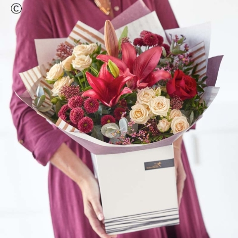 bouquet of blooms in red and green, with peach and cream highlights and pops of burgundy and cerise