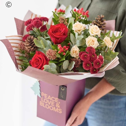 festive gift box with blooms in red and green, with peach and cream highlights and pops of burgundy and cerise