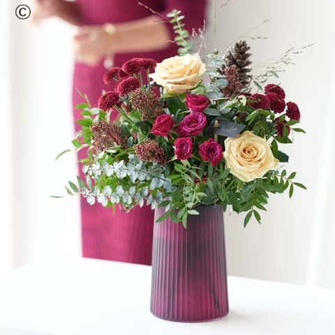 transparent ribbed handblown vase with blooms in red and green, with peach and cream highlights and pops of burgundy and cerise