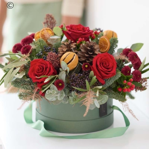 big hatbox of Christmas flowers, featuring blooms in red and green, with peach and cream highlights and pops of burgundy and cerise