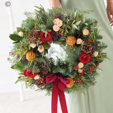 a luxurious christmas wreath, featuring blooms and foliage in shades of red and green, with peach and cream highlights and pops of burgundy and cerise